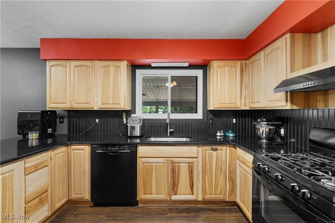 Kitchen featuring black appliances, light brown cabinetry, a textured ceiling, dark wood-type flooring, and dark stone countertops