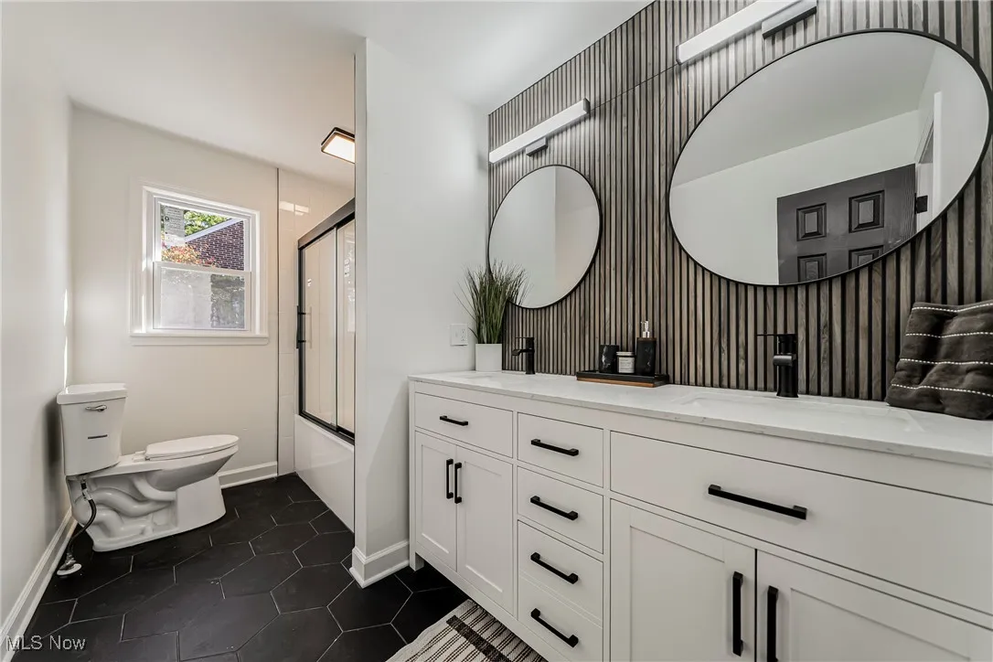 Bathroom featuring double vanity, combined bath / shower with glass door, and dark tile patterned floors