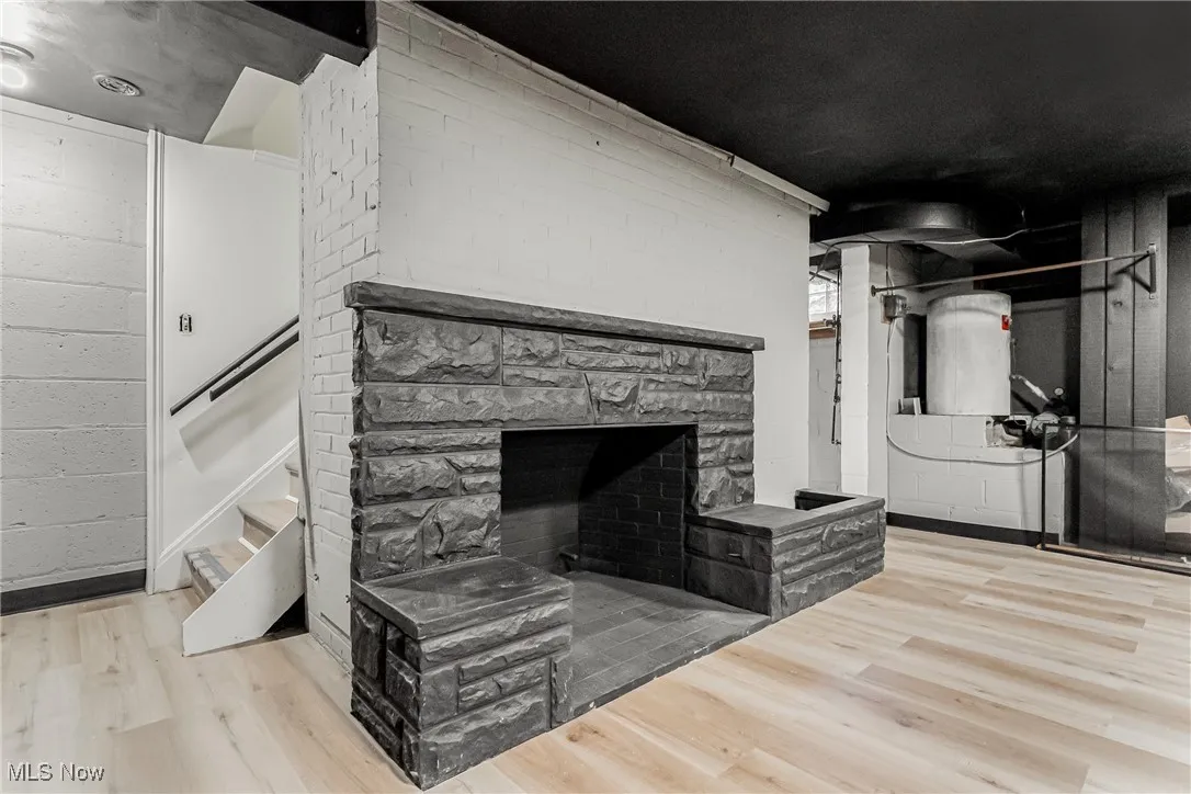 Unfurnished living room with a fireplace, light wood-style flooring, stairs, and concrete block wall
