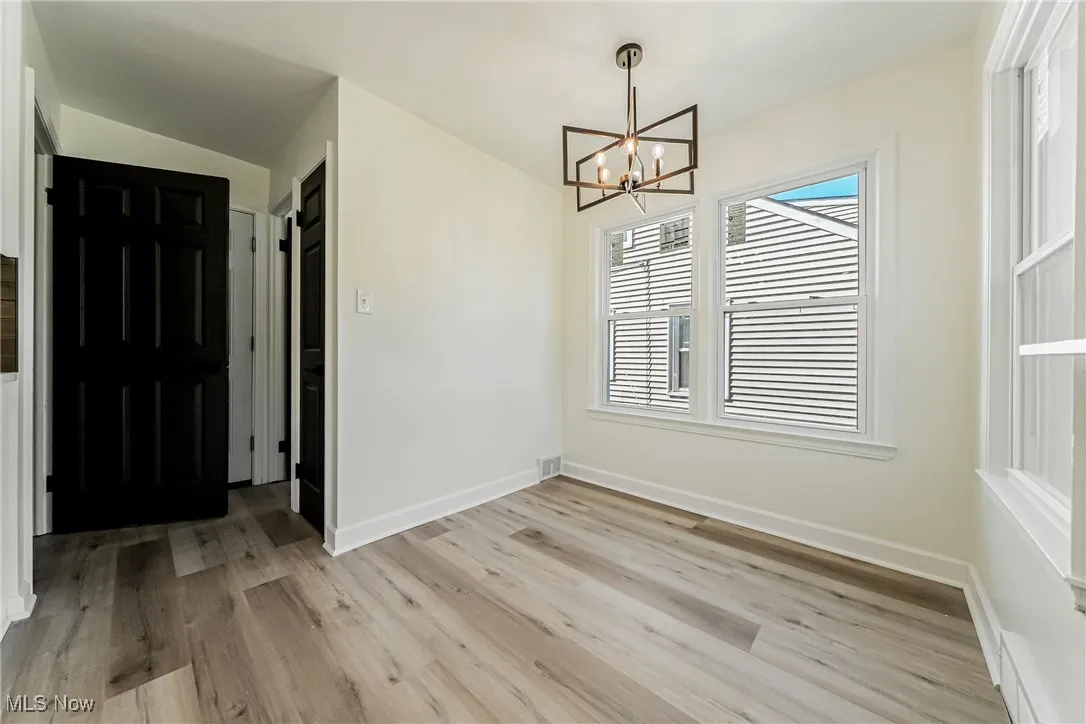 Unfurnished dining area with light wood-style flooring, a chandelier, and lofted ceiling