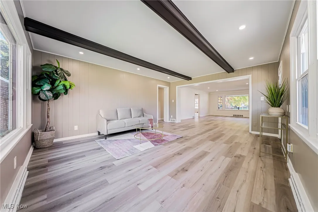Living area featuring beamed ceiling, wood walls, a baseboard radiator, light wood finished floors, and recessed lighting