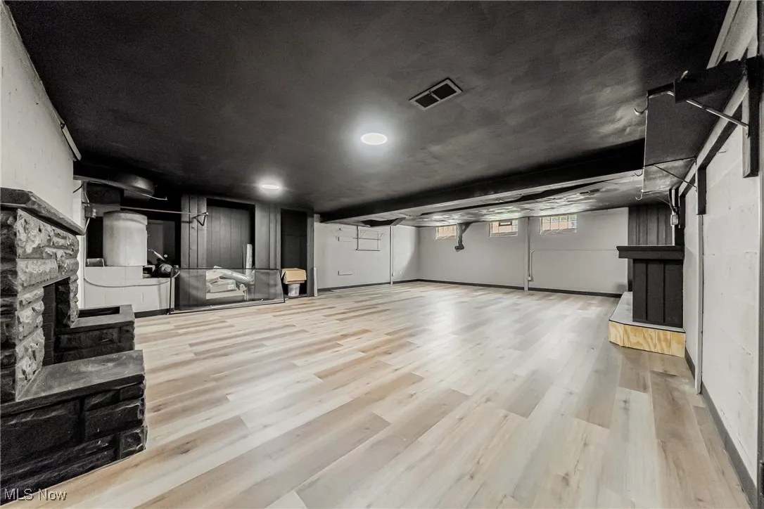 Basement with a stone fireplace, light wood finished floors, and concrete block wall