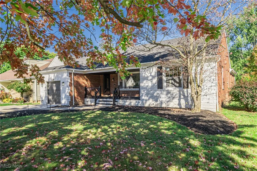 View of front of house with a front yard, brick siding, covered porch, and an attached garage