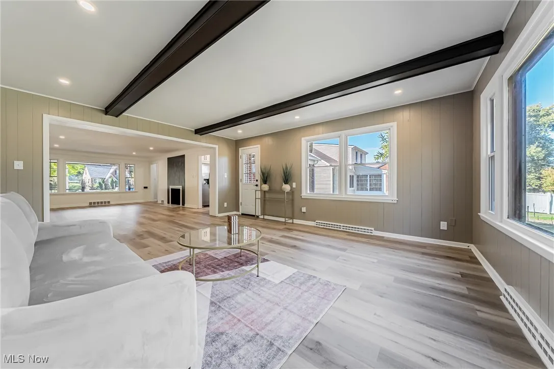 Unfurnished living room featuring beamed ceiling, a baseboard heating unit, light wood finished floors, wooden walls, and recessed lighting