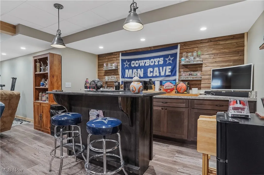 Indoor bar featuring light wood-style floors, decorative light fixtures, recessed lighting, and wood walls