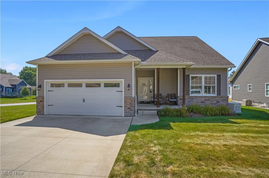 View of front of house featuring stone siding, a front yard, a shingled roof, driveway, and an attached garage