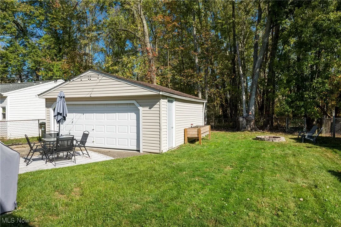 View of detached 2-car garage, patio, fire pit and fenced backyard