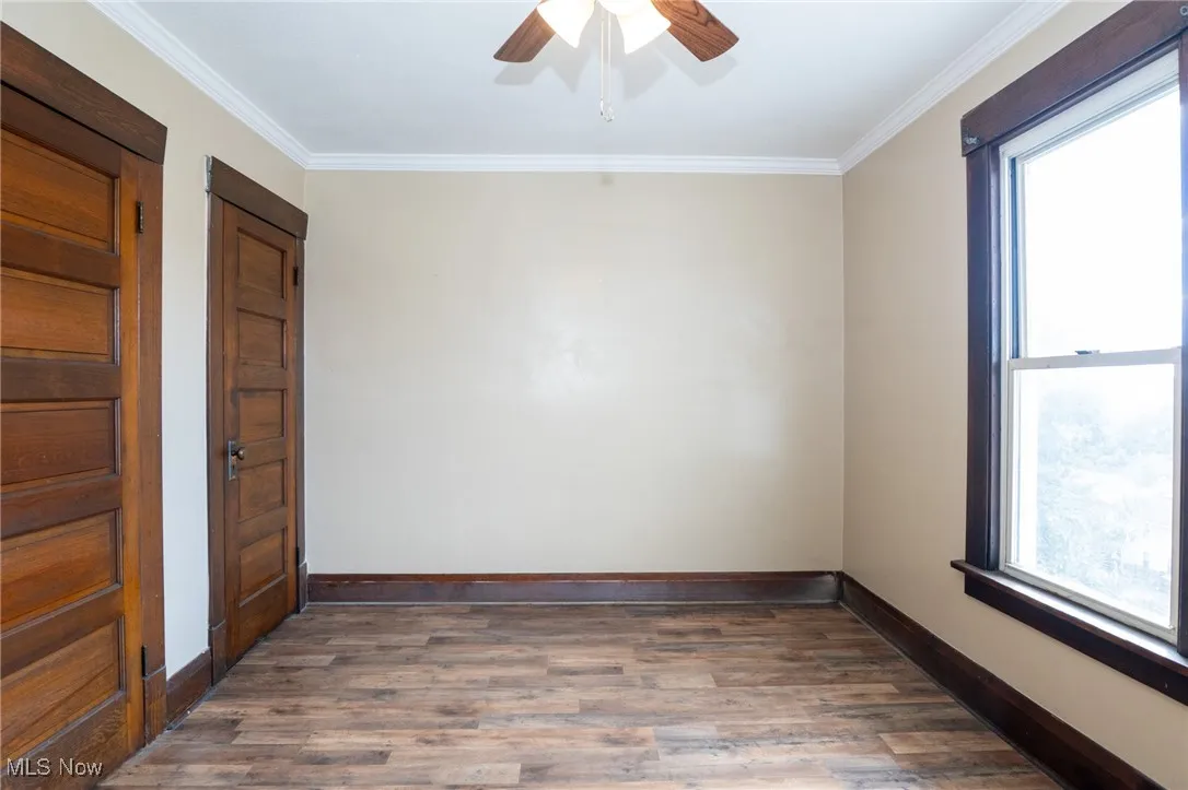 Empty room with dark wood-type flooring, ornamental molding, and a ceiling fan