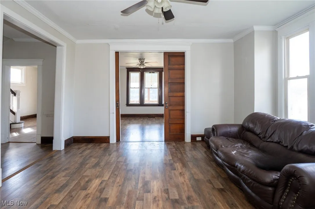 Living room featuring healthy amount of natural light, dark wood-type flooring, crown molding, and ceiling fan