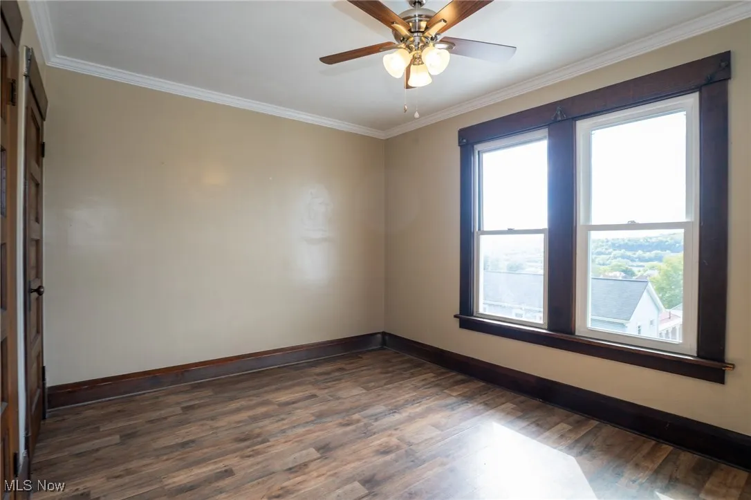 Empty room with ornamental molding, dark wood-style flooring, and ceiling fan