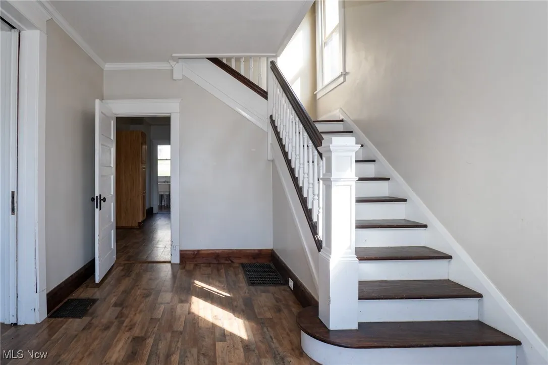Stairway featuring wood finished floors and crown molding