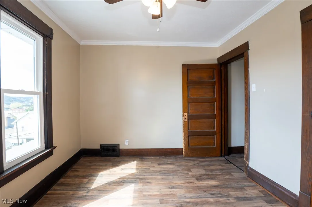 Unfurnished room with ornamental molding, dark wood-type flooring, and ceiling fan