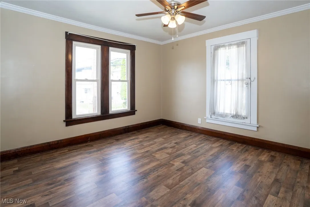Spare room with crown molding, plenty of natural light, dark wood-style flooring, and ceiling fan