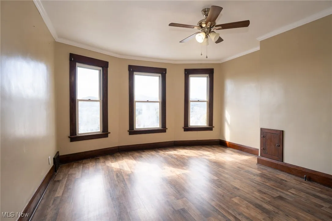 Unfurnished room with plenty of natural light, ornamental molding, dark wood-style flooring, and ceiling fan