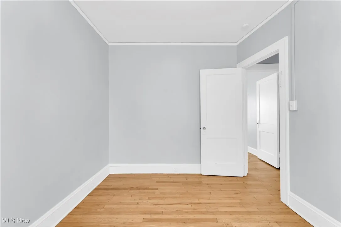 Empty room featuring light wood-type flooring and crown molding