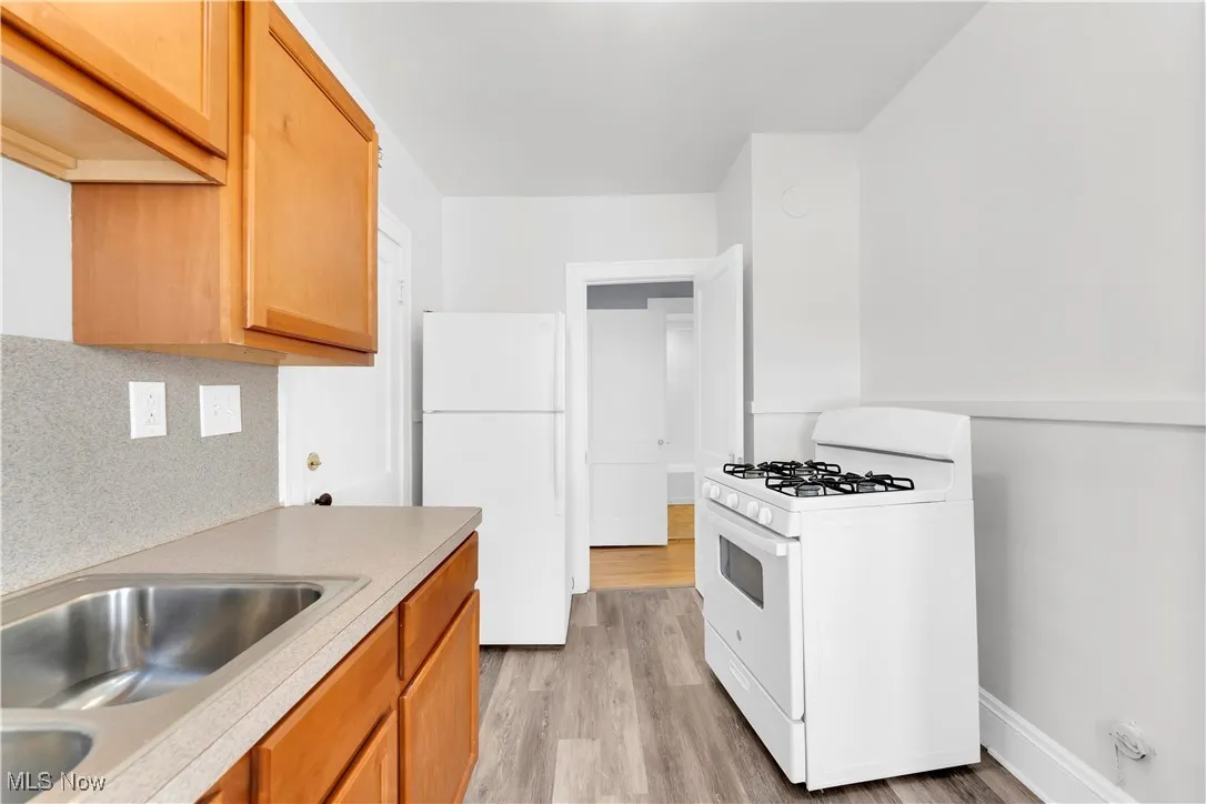 Kitchen featuring white appliances, light wood-style floors, decorative backsplash, light countertops, and brown cabinets