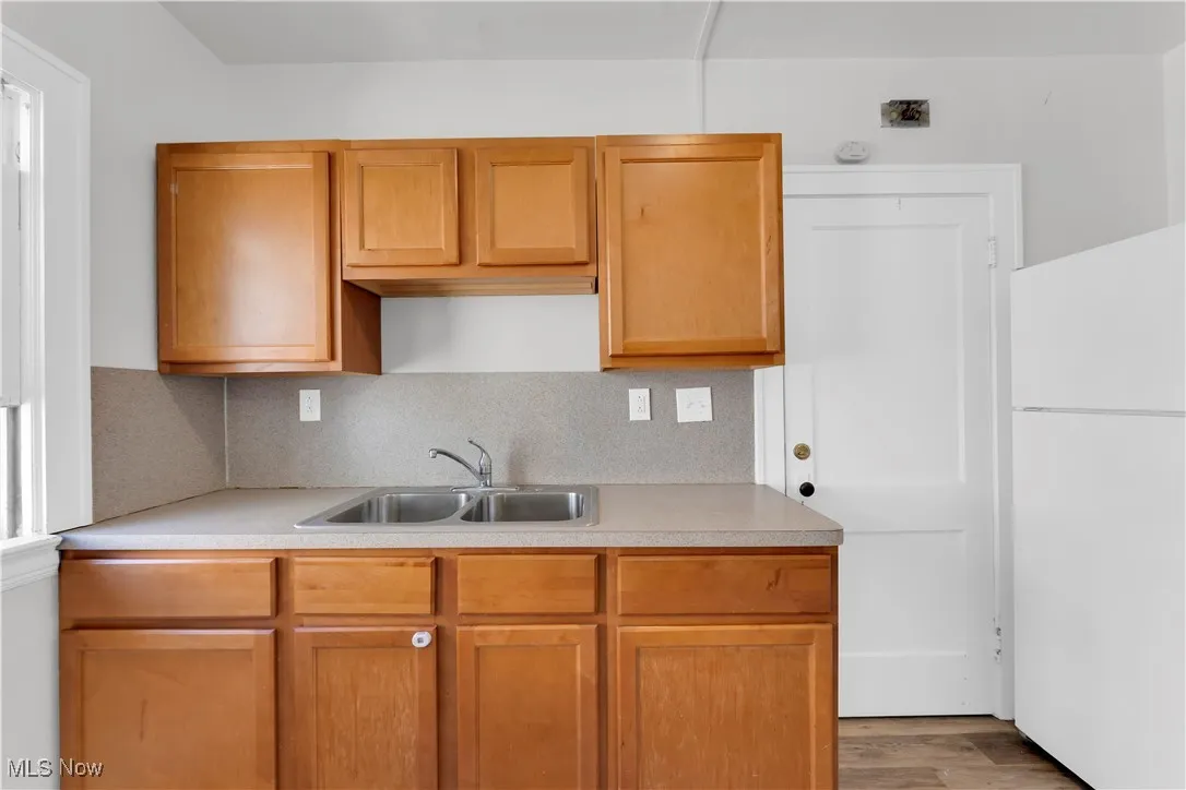 Kitchen featuring freestanding refrigerator, light countertops, wood finished floors, backsplash, and brown cabinets