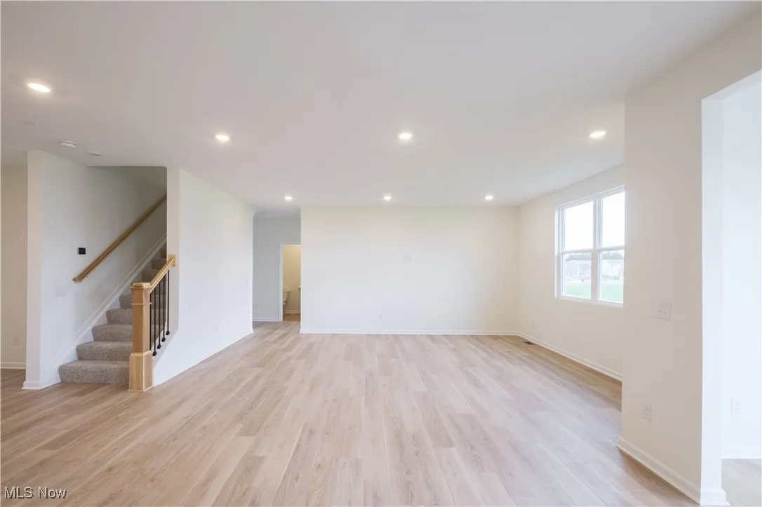 Unfurnished living room featuring stairway, light wood finished floors, and recessed lighting
