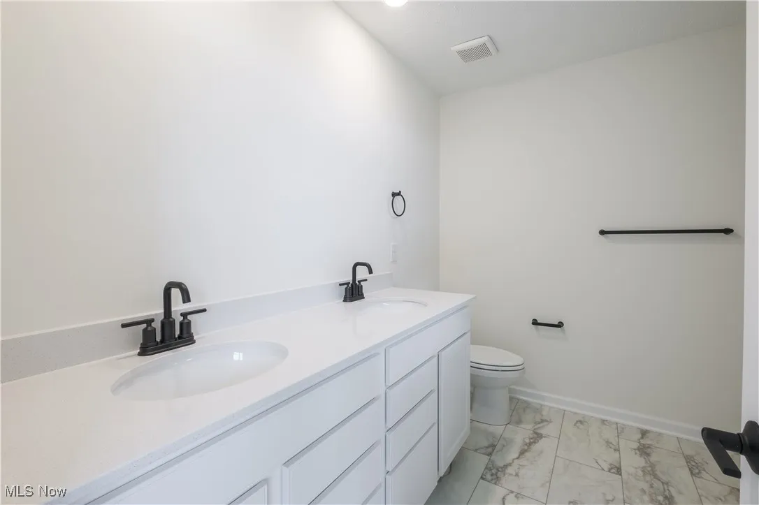 Bathroom with double vanity and light marble finish flooring
