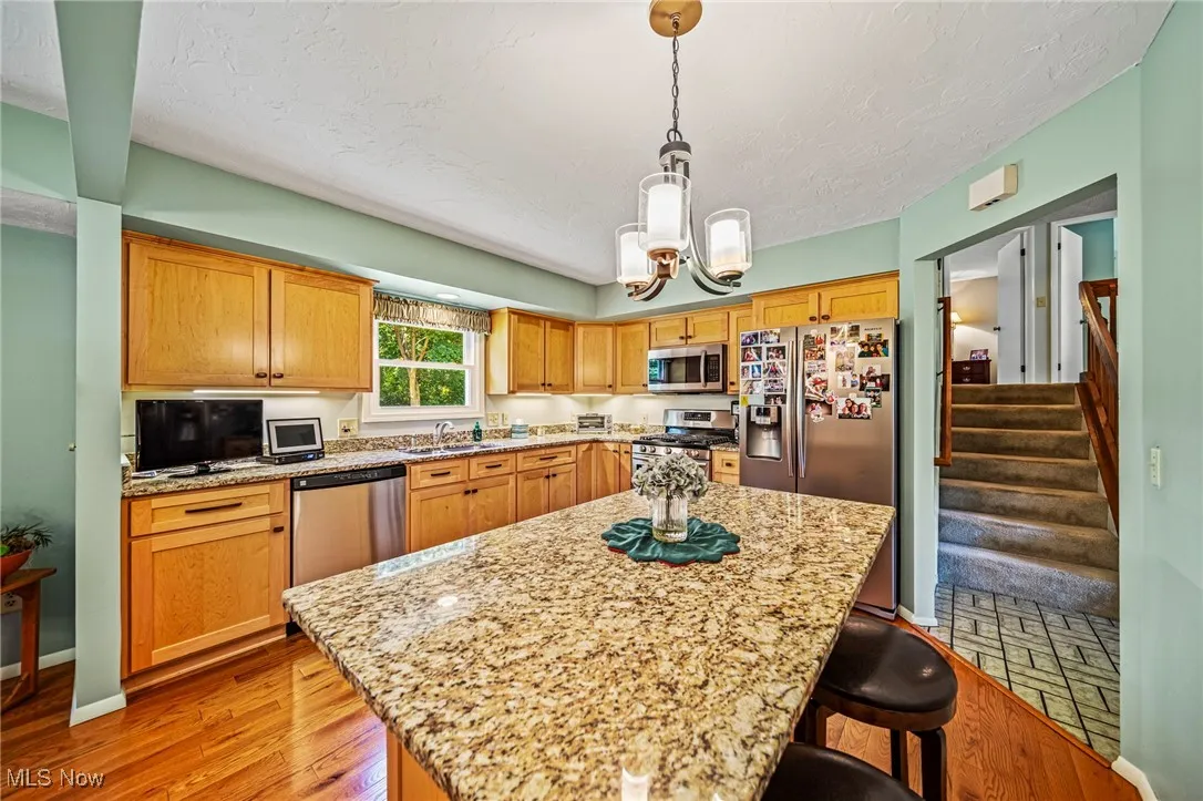 Kitchen featuring a breakfast bar, a textured ceiling, hanging light fixtures, stainless steel appliances, and light stone countertops