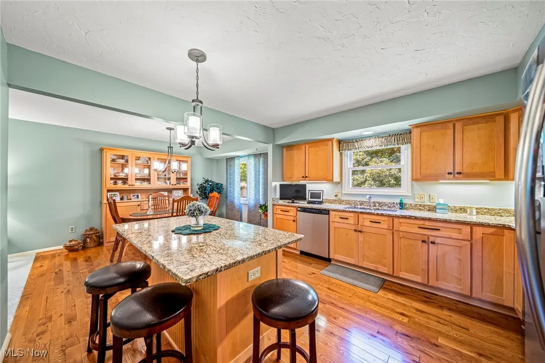 Kitchen featuring light stone countertops, light wood-style floors, a breakfast bar area, a center island, and a chandelier