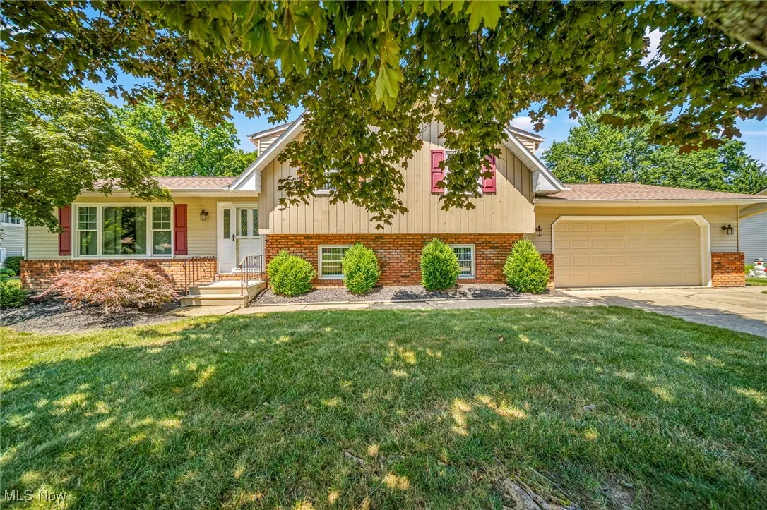 Split level home with an attached garage, a front yard, driveway, and brick siding
