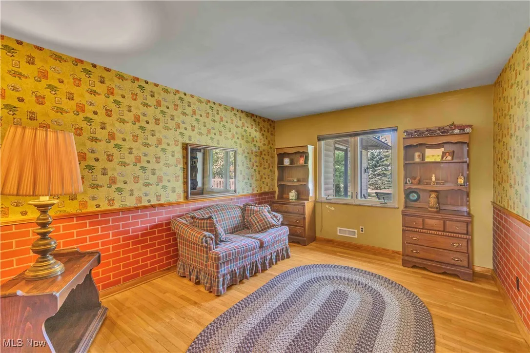First bedroom of the hall with ornate wallpaper, window, closet and hardwood floors.