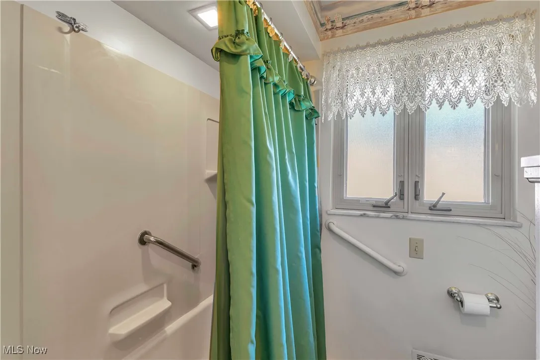 Full bathroom in the hall with a window for natural light, large updated vanity with two mirrors above, shower/bath combo with shower curtain, and light tile floors.