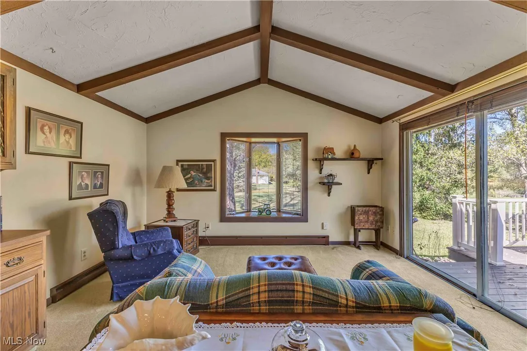 Family room with vaulted, beamed ceilings, bay window, sliding door to the back deck and light colored carpeting.