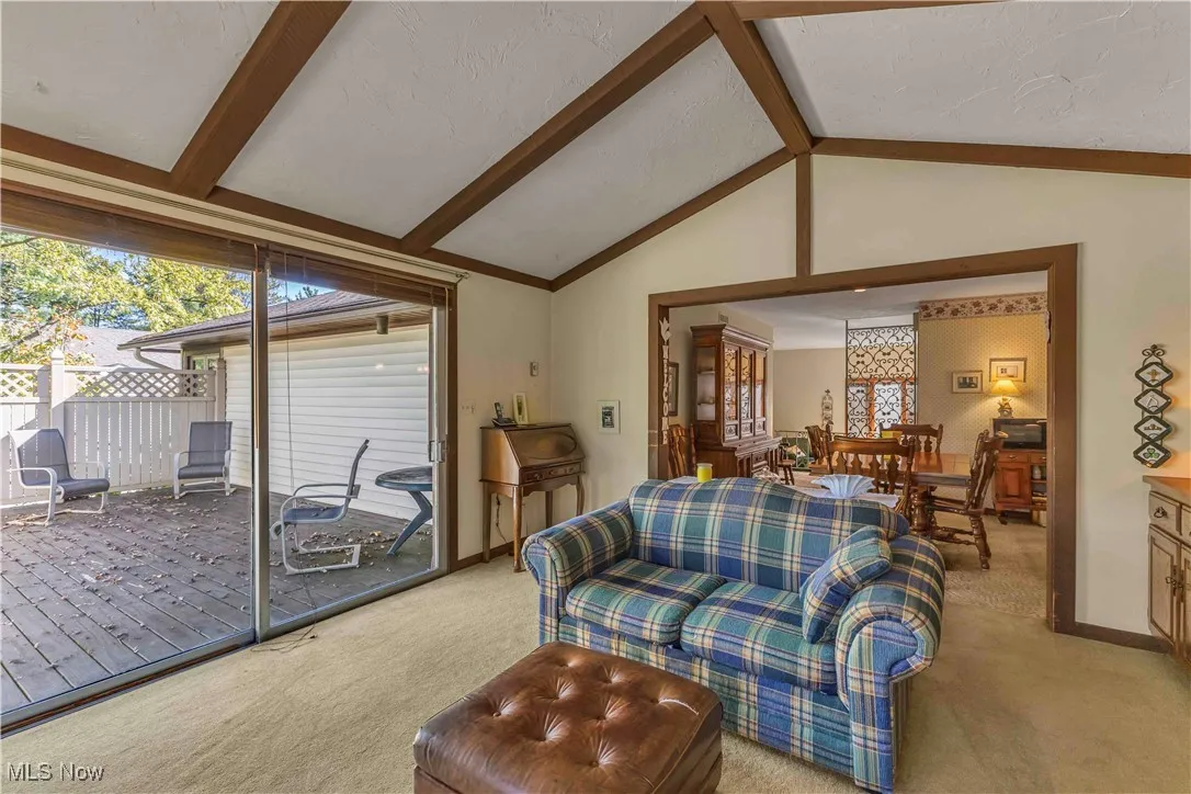 Family room with vaulted, beamed ceilings, bay window, sliding door to the back deck and light colored carpeting.