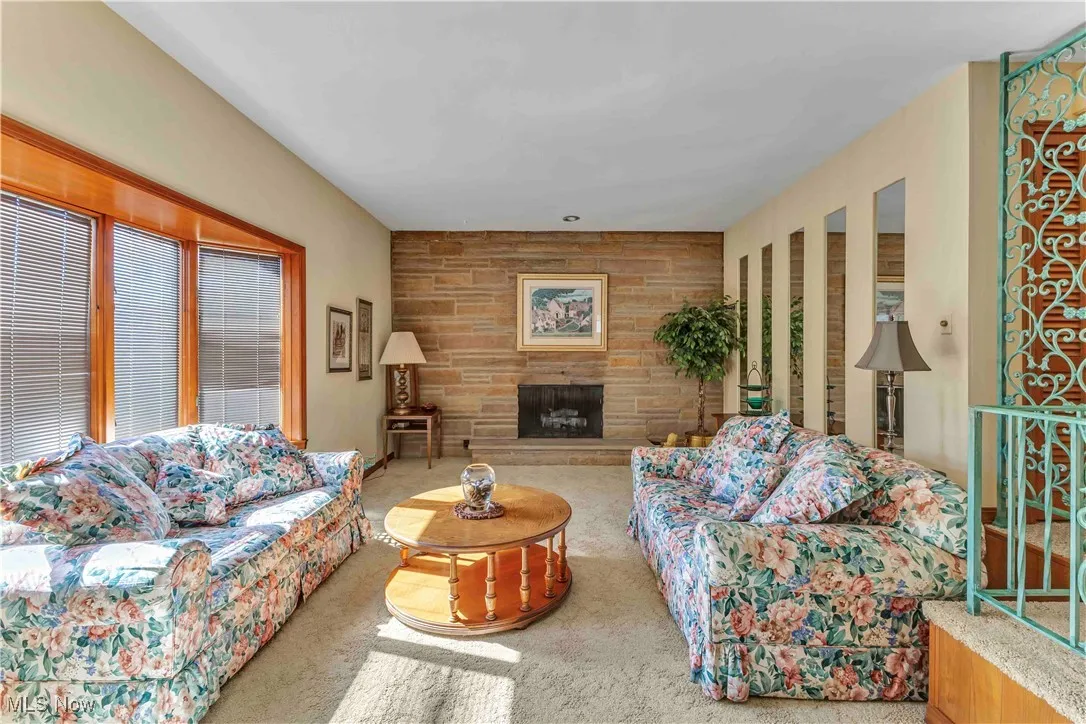 Living room boasting stone faced fireplace and light carpeting.