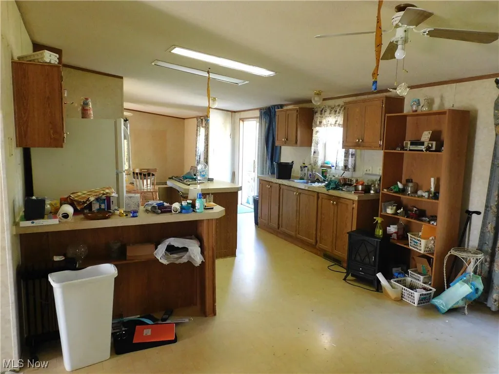 Kitchen with freestanding refrigerator, brown cabinets, light countertops, and open shelves
