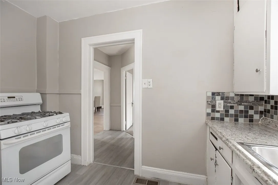Kitchen with white range with gas cooktop, light countertops, white cabinetry, backsplash, and light wood finished floors