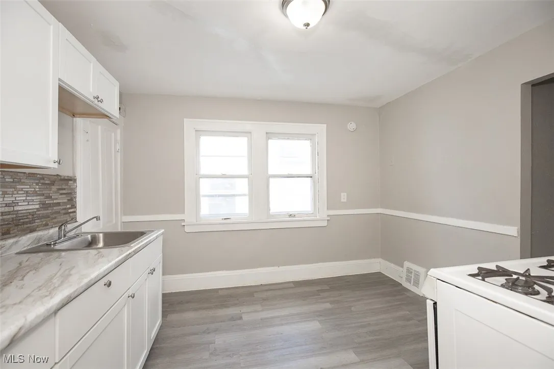 Kitchen with white cabinets, backsplash, light countertops, light wood-style floors, and gas range gas stove