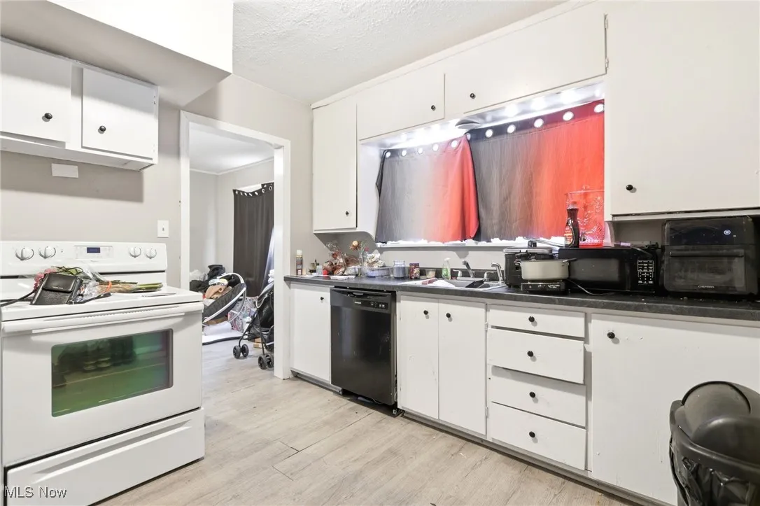 Kitchen with black appliances, light wood-style flooring, white cabinetry, dark countertops, and a textured ceiling