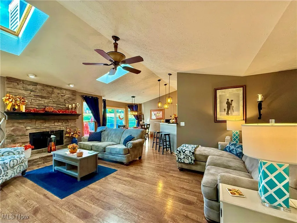 Living room with 2 skylights, vaulted ceiling, brick gas fireplace, and ceiling fan
