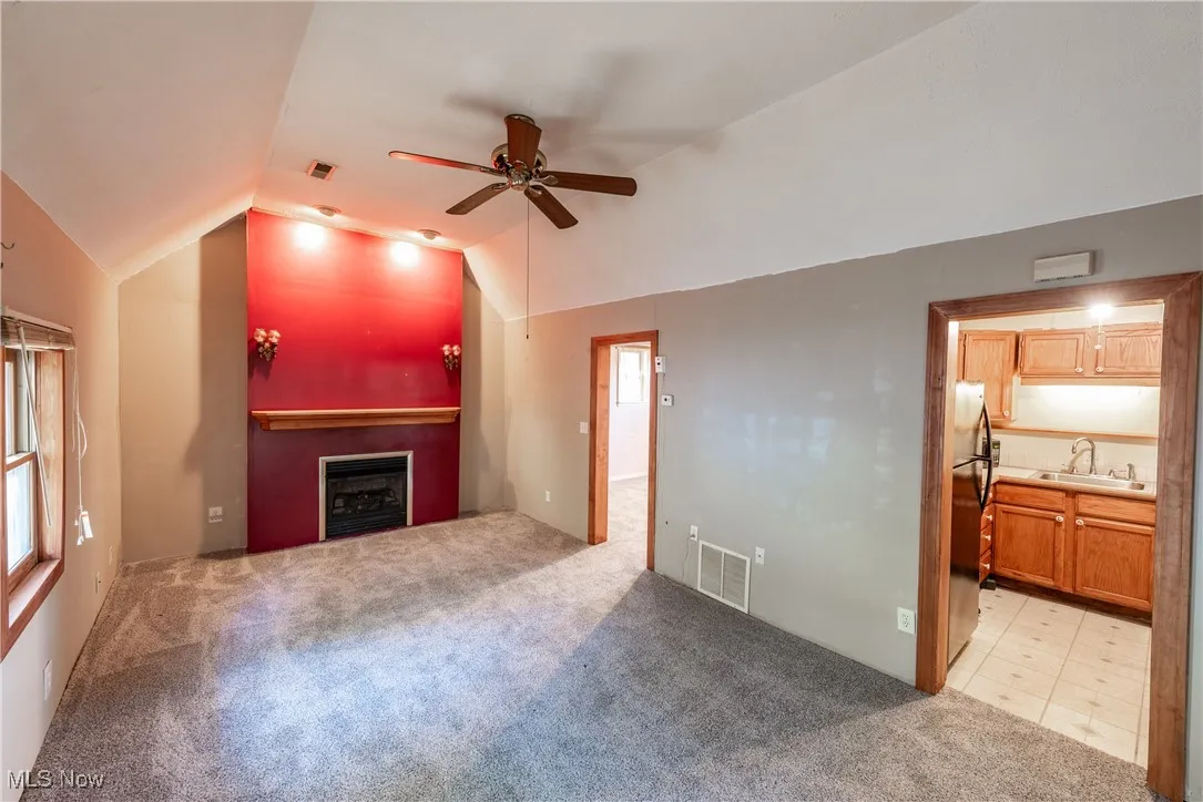 Cottage living room with light colored carpet, lofted ceiling, ceiling fan, and a fireplace