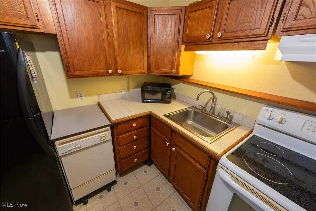 Cottage Kitchen with white appliances, brown cabinetry, under cabinet range hood, and tile counters