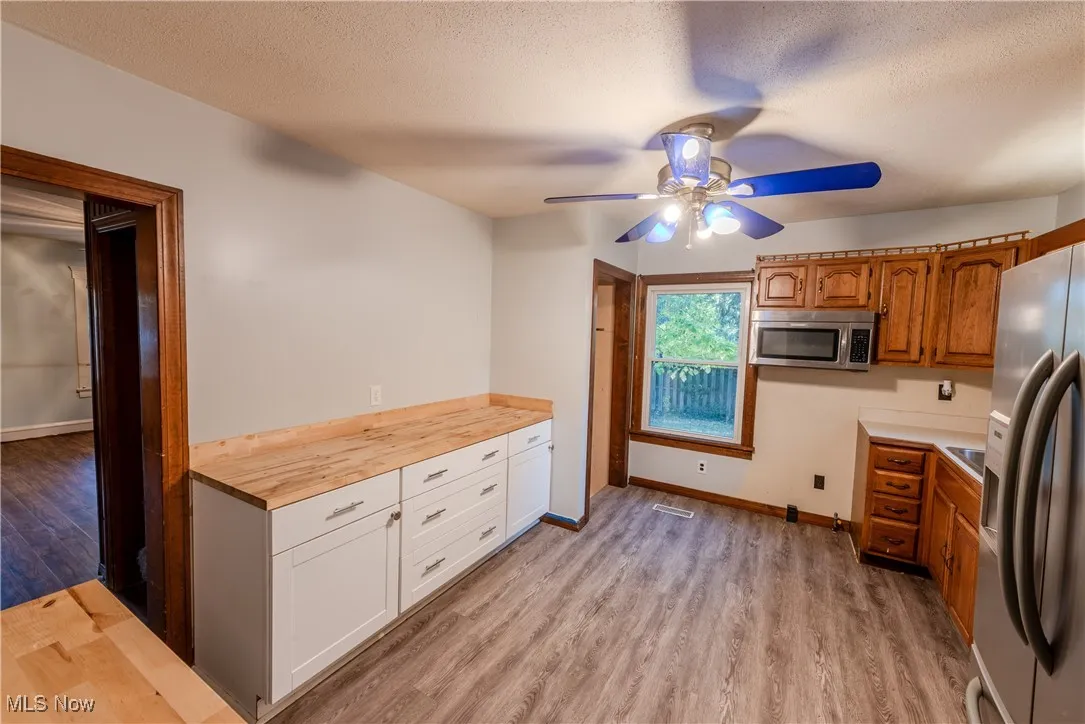 Kitchen with appliances with stainless steel finishes, light wood-style floors, wooden counters, a textured ceiling, and a ceiling fan