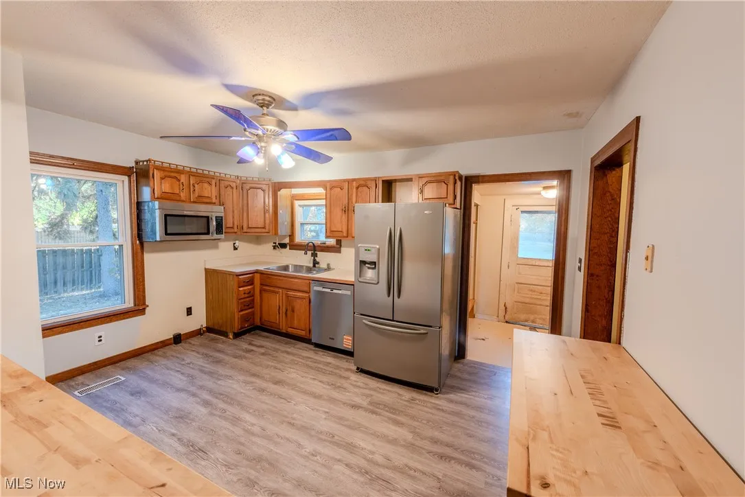 Kitchen with stainless steel appliances, light wood-style flooring, brown cabinets, ceiling fan, and butcher block countertops