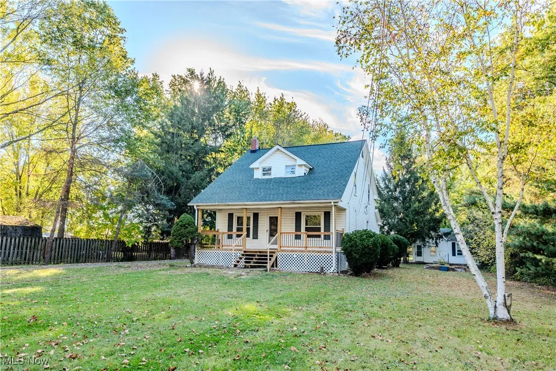 View of front of house with covered porch, a chimney, a fenced backyard, a shingled roof, and view of wooded area