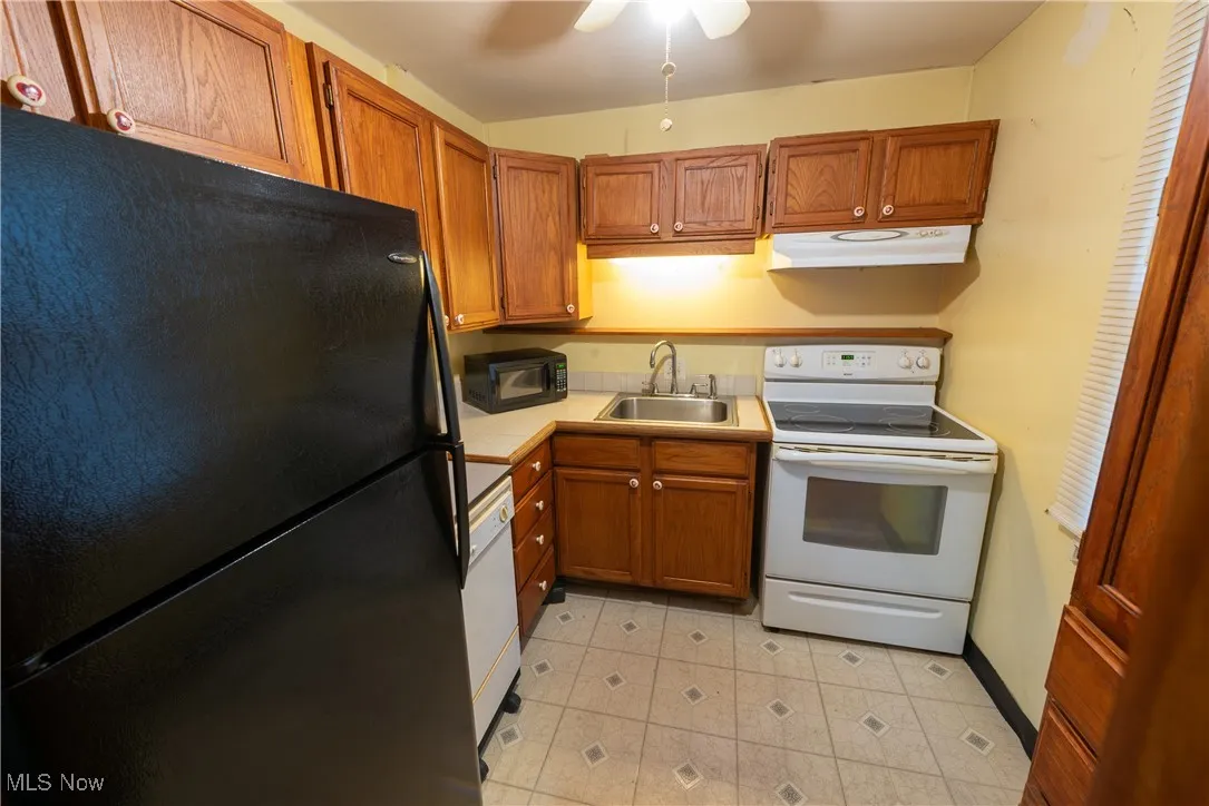 Cottage Kitchen featuring black appliances, countertops, brown cabinets, under cabinet range hood, and ceiling fan