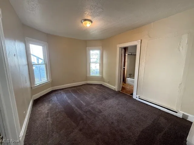 Apartment 2 Unfurnished room with a textured ceiling, dark carpet, and baseboard heating