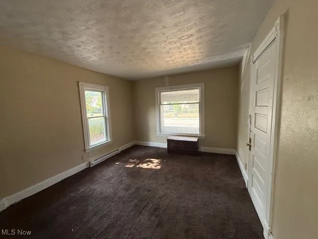 Apartment 2 Unfurnished room with dark carpet, a textured ceiling, multiple windows, and a baseboard heating unit