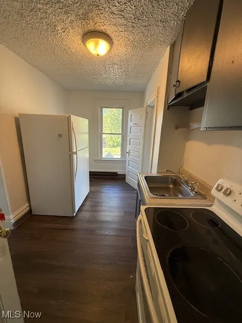 Apartment 3 Kitchen with white stove, refrigerator, dark wood-type flooring, a textured ceiling, and light countertops