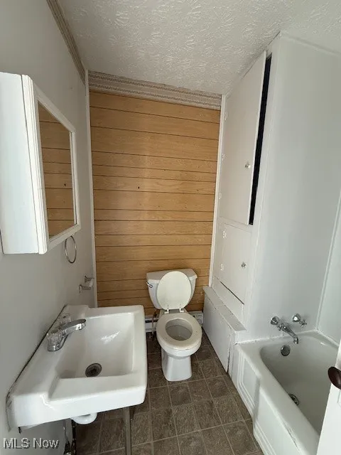 Apartment 4 Full bathroom featuring a textured ceiling, wood walls, shower / bath combination, and dark tile patterned flooring
