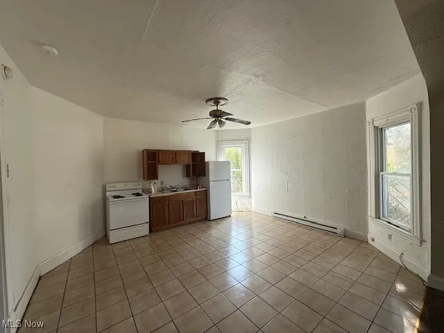 Apartment 2 Kitchen with white appliances, brown cabinetry, a ceiling fan, a baseboard radiator, and light countertops