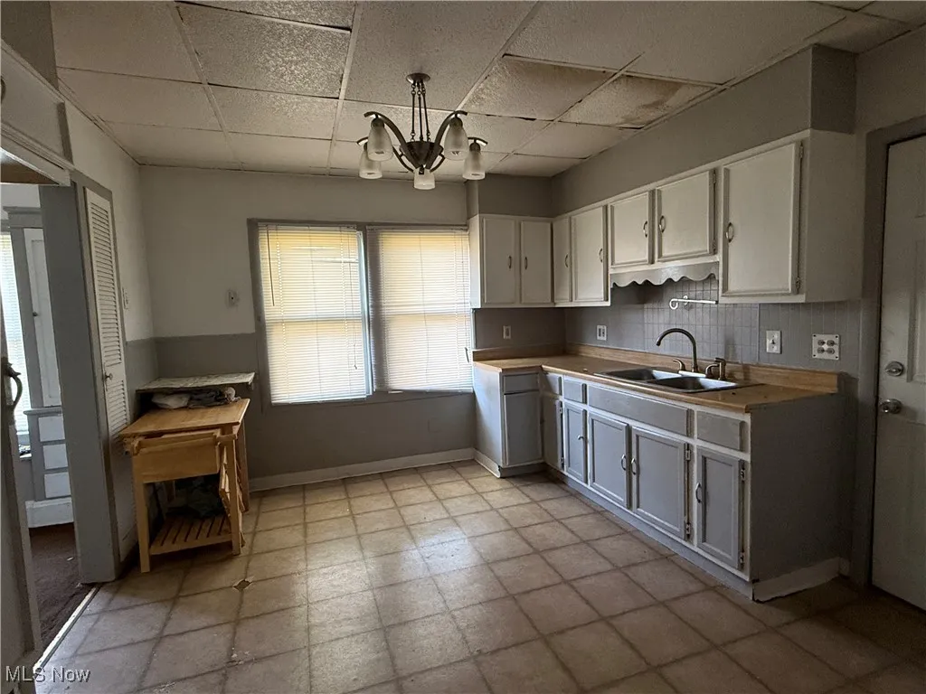 Kitchen with a paneled ceiling, white cabinetry, light countertops, a chandelier, and decorative backsplash