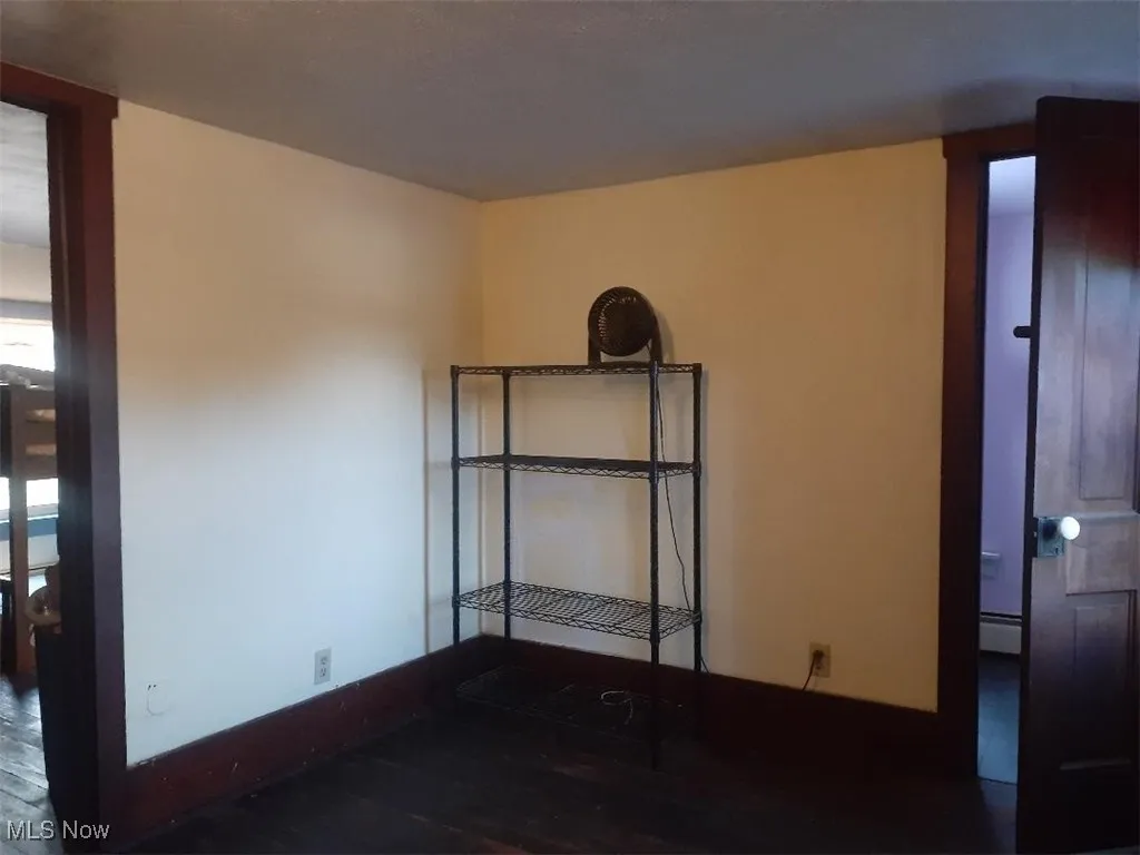 Empty room with dark wood-type flooring and a baseboard heating unit
