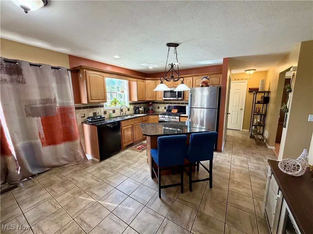 Kitchen with a center island, a breakfast bar area, dark stone counters, appliances with stainless steel finishes, and hanging light fixtures